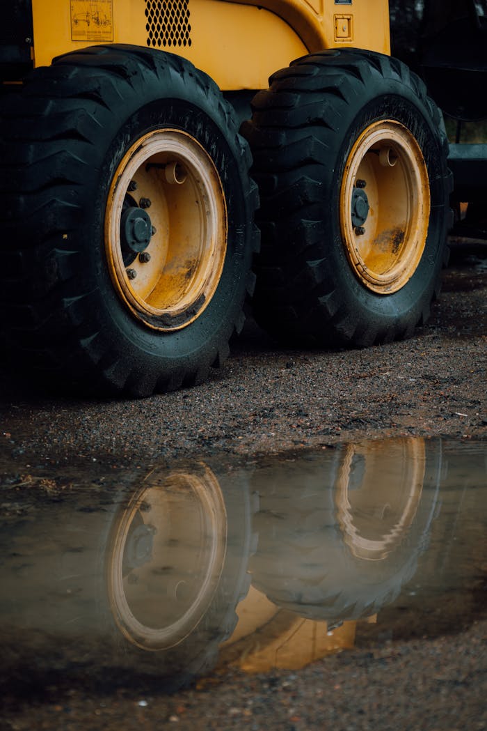 Close-up view of large machinery tires reflected in a puddle. Atmospheric industrial setting.